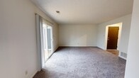 Located at 5004 S Webster St in Kokomo, Indiana, Unit C is a single-floor residence that offers a practical and comfortable layout. The main living area is generously sized, featuring neutral-toned carpet and crisp white walls that create a clean, open atmosphere. A full-width sliding glass door floods the space with natural light and provides direct access to a wooden deck, which overlooks a pleasant outdoor setting with mature trees — a welcoming extension of the living space.

The kitchen is equipped with warm oak cabinetry, golden-toned countertops, and a white electric range with an overhead ventilation hood, providing a functional cooking environment with ample storage. The bathroom features a full-size tub and shower combination with built-in shelving niches and chrome fixtures, finished in a clean, neutral palette.

The bedrooms are carpeted and well-proportioned, each offering a calm, neutral backdrop. One bedroom benefits from a large window with views of the surrounding neighborhood, allowing for excellent natural light throughout the day. The textured ceilings and consistent neutral tones throughout the unit contribute to a cohesive and move-in-ready aesthetic. The overall layout, as seen from the dollhouse view, is efficient and logically organized for everyday living.