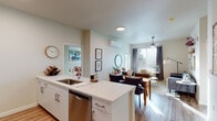 This single-floor residence at 3224 SW 12th Ave in Portland, Oregon, features a thoughtfully designed open-concept layout that seamlessly connects the kitchen, dining, and living areas. The kitchen is outfitted with white cabinetry, quartz countertops, a central island with an undermount sink, and a full suite of stainless steel appliances, including a side-by-side refrigerator, electric range, built-in microwave, and dishwasher. A wall-mounted mini-split system provides climate control throughout the main living area.

The living room receives natural light through large windows dressed with blinds and floor-length drapes, creating a bright yet comfortable atmosphere. Hardwood-style flooring runs throughout the main living spaces, adding warmth and visual continuity.

The unit includes two bedrooms, each with ceiling fans, natural light, and carpeted flooring. Both bathrooms are finished with white vanities, quartz countertops, large mirrors, and tub-shower combinations with tile surrounds.

A dedicated laundry room houses a full-size Whirlpool washer and dryer alongside wire shelving for additional storage. The overall design emphasizes clean lines, neutral tones, and functional living in a well-appointed Portland location.