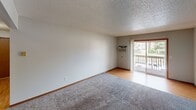 This single-floor unit offers a well-organized layout designed for comfortable everyday living. The living area is generously sized, featuring plush carpet flooring, neutral-toned walls, a textured ceiling, and a sliding glass door that opens to a private balcony with outdoor views — allowing natural light to fill the space. A window-mounted air conditioning unit provides climate control.

The kitchen is equipped with warm oak cabinetry offering ample storage, light-toned countertops, a double stainless steel sink, and a dishwasher. Tile flooring and under-cabinet lighting contribute to a functional and practical cooking environment. A refrigerator is included.

The unit includes two carpeted bedrooms, each featuring windows that bring in natural light and baseboard heating. One bedroom includes a built-in closet with a hanging rod for convenient storage, with direct access to the kitchen area visible from the hallway.

The bathroom features tile flooring, a built-in tub and shower combination, a wall-mounted towel bar, a toilet, and a vanity with countertop space. The layout is clean and efficient. Throughout the unit, warm wood-tone trim and doors provide a cohesive design element, while textured ceilings and neutral walls create a bright, understated ambiance.
