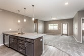 This single-floor residence showcases a cohesive modern design with neutral gray and taupe tones throughout. The open-concept kitchen serves as the focal point, featuring a large center island with granite countertops and a stainless steel double sink illuminated by pendant lights. Dark espresso cabinetry lines the walls, complemented by stainless steel appliances including a refrigerator, range, and microwave. Wood-look flooring extends through the kitchen and entry areas, providing a warm contrast to the soft carpet found in the living and bedroom spaces.

The living area is generously sized, offering an open layout with a closet and windows that bring in natural light. Bedrooms continue the carpeted flooring and neutral palette, with windows overlooking the exterior and ceiling fans for added comfort. Multiple windows across the unit ensure consistent natural light throughout.

The bathrooms feature granite-topped dark vanities with wood-look flooring, and one includes a full tub-shower combination with chrome fixtures. A dedicated walk-in closet with built-in shelving and rods is accessible from one of the bathrooms, providing practical storage. A laundry area is also present within the unit. Overall, the space presents a clean, functional layout with consistent modern finishes.