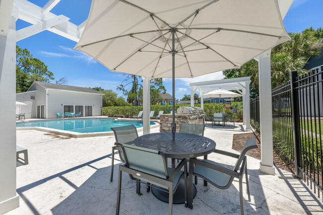 Inviting outdoor pool area featuring comfortable seating under umbrellas, modern grill, and lush greenery, perfect for relaxation and entertaining. - Vista North