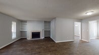 Located at 500 Bridle Ridge Ln in Raleigh, North Carolina, this single-floor home offers a well-organized layout with a neutral gray color palette and a mix of hardwood-style and carpeted flooring throughout. The living room serves as the centerpiece of the home, showcasing a classic tile-surround fireplace flanked by symmetrical built-in shelving units — ideal for display or storage. Dark hardwood-style flooring anchors the space, and natural light enters through a window on the adjacent wall. The open layout connects seamlessly to additional common areas, providing a smooth flow throughout the home. The kitchen is efficiently designed with white cabinetry extending to the ceiling for generous storage, white countertops, and wood-look flooring. Black appliances, including a refrigerator and range, provide a clean contrast against the bright cabinetry. The bedrooms feature plush carpeting and include walk-in closets for added storage. The primary bedroom benefits from sliding glass doors that open to an outdoor view, bringing in abundant natural light. Bathrooms are functional and clean, featuring a tub-shower combo with built-in shelving. Throughout the home, textured ceilings and crisp white trim complement the soft gray walls, creating a cohesive and inviting atmosphere.