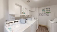 Located at 951 S Oxford Ave in Los Angeles, CA, this shared laundry facility offers a clean, well-organized space designed for practical, efficient use. The room features a lineup of multiple top-load washing machines and dryers arranged along the walls, providing ample capacity for building residents. A wall-mounted shelf runs the length of the machine lineup, offering a convenient surface for folding or staging laundry. The flooring throughout is wood-look laminate, lending a tidy, contemporary appearance that is easy to maintain. The walls are finished in crisp white, and overhead ventilation ensures proper airflow throughout the space. Usage instructions and informational guides are clearly posted on the walls, making machine operation straightforward for all users. A fire extinguisher is visibly mounted for safety compliance. The room is accessed through a labeled door and is conveniently situated near an elevator, enhancing accessibility for all building residents. Overall, the space is efficiently laid out, well-lit, and maintained to a clean standard, providing a functional and accessible laundry solution for the building at large.