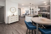This single-story residence is designed with a contemporary aesthetic, combining functionality and style across its well-appointed layout. The open-concept kitchen serves as a central hub, featuring granite countertops, a large island with bar seating illuminated by sleek pendant lighting, dark taupe cabinetry, stainless steel appliances, and wood-look plank flooring that extends throughout the main living areas. A compact dining nook adjacent to the kitchen provides additional seating options.

The living room offers a comfortable, functional layout with access to natural light through large windows and a glass-paneled exterior door. Recessed lighting and neutral walls create a bright, versatile atmosphere.

The primary bedroom is generously sized with plush carpeting, multiple windows offering outdoor views, a ceiling fan, and direct access to an en-suite bathroom. The primary bath includes a granite-topped double vanity with dark cabinetry, tile flooring, and a walk-in glass-door shower. A second bedroom, also carpeted and well-lit, is accompanied by a full bathroom featuring a granite vanity, tile flooring, and a shower-tub combination. The unit also includes an in-unit utility closet and ample interior door detailing throughout.