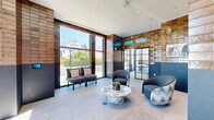 Located at 165 North St in Stamford, CT, this thoughtfully designed single-floor pet amenity space combines a comfortable lounge area with a professional-grade grooming kitchen. The living room area makes an immediate impression with its striking two-tone wall treatment — warm, rustic brick cladding on the upper half transitions into sleek navy blue tile on the lower half, creating a bold industrial-modern aesthetic. Large floor-to-ceiling windows flood the space with abundant natural light and offer views of the surrounding streetscape. The polished stone tile flooring, modern seating, and a sculptural marble-topped coffee table contribute to a refined yet welcoming atmosphere. A built-in wet bar with teal mosaic tile backsplash, dark cabinetry, and a stainless steel mini fridge adds a functional yet stylish focal point to the lounge. The adjacent grooming kitchen is fully equipped with professional stainless steel bathing stations, multiple utility sinks with flexible hose attachments, and ample counter space, all set against clean white wall tile and the same stone flooring. Playful framed dog portraits add a lighthearted character to the grooming area. This well-appointed space delivers a premium experience for pets and their owners alike.