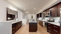 Located at 912 Innovation Way in Altamonte Springs, Florida, this single-floor model unit offers an efficient and well-appointed layout that demonstrates smart use of space. The open-concept design seamlessly integrates the kitchen and bathroom areas under a crisp white ceiling with recessed lighting, creating a bright and welcoming atmosphere throughout.

The kitchen is a standout feature, boasting rich dark espresso cabinetry that extends from floor to ceiling, providing ample storage. A central island with a granite countertop serves as both a prep surface and a visual anchor for the space. Stainless steel appliances — including a refrigerator with ice and water dispenser, electric range, over-the-range microwave, and dishwasher — deliver a polished, modern aesthetic. A light gray subway tile backsplash adds texture and contrast against the dark cabinetry, while light wood-toned luxury vinyl flooring runs throughout, tying the space together.

Adjacent to the kitchen, the bathroom area features a matching dark vanity with granite countertops, a large framed mirror, and a full soaking tub with shower combination set within a clean white surround. The layout is practical and cohesive, with a closeted area and additional doors providing privacy and utility. Recessed lighting ensures the entire space remains well-lit and functional.