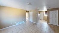 This single-floor apartment at Sanford Estates offers a practical and comfortable layout designed for everyday living. The entry area welcomes residents into a spacious main living space featuring light-toned ceramic tile flooring, warm beige walls, and a textured ceiling. A baseboard heating unit runs along the wall, and the open flow of the space connects seamlessly to the kitchen and adjacent rooms.

The kitchen is equipped with oak cabinetry, a double coil electric range, a full-size refrigerator, and a single-basin sink set into dark-toned countertops. Tile flooring continues throughout this area, and a door provides convenient access to the exterior.

Multiple bedrooms are finished with plush carpeting in a warm brown tone, neutral beige walls, and windows fitted with vertical blinds that allow natural light to filter in while maintaining privacy. Each room features a textured ceiling and is well-proportioned to accommodate standard furnishings.

The bathroom includes a full tub-shower combination with a grab bar, tiled surround, a toilet, and a pedestal-style vanity sink beneath a large mirror with overhead vanity lighting. Vertical blinds on the bathroom window add privacy while allowing light into the space.

Overall, this apartment presents a clean, functional interior with consistent neutral tones and practical finishes throughout.