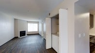 This 1-bedroom, 1-bathroom unit offers a thoughtfully designed single-floor layout that balances functionality and modern style. The open living area is anchored by a sleek fireplace, creating a warm and inviting focal point, while a large window allows natural light to fill the space and brighten the interior. Rich dark hardwood-style flooring runs throughout, providing a clean contrast against the crisp white walls and ceilings. A dedicated in-unit laundry closet is neatly integrated into the hallway, complete with a washer and built-in shelving above for additional storage — a practical convenience that adds everyday comfort. The neutral color palette and clean architectural lines give the unit a contemporary feel that is both modern and welcoming. The corridor connects the living area to the private spaces, offering a well-organized flow. Overall, this unit combines essential amenities with a clean, minimalist aesthetic, making it a comfortable and functional living space suited for a variety of lifestyles.