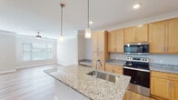This single-floor residence in Clayton, NC offers a thoughtfully designed open-concept layout that connects the kitchen and living areas seamlessly. The kitchen is a standout feature, showcasing light maple cabinetry extending to the ceiling, granite countertops, and a full suite of stainless steel appliances including a range, built-in microwave, and French door refrigerator. A central island with an undermount sink and pendant lighting above provides both additional workspace and a natural gathering point. Crown molding frames the kitchen and living areas, adding a refined architectural detail throughout.

The living area is finished with light hardwood flooring and features a ceiling fan, recessed lighting, and multiple windows dressed with blinds that allow generous natural light. A set of French doors with a transom window above opens to the exterior, enhancing the sense of openness. A built-in bench and cabinetry nook adds functional storage near the kitchen transition.

The bedroom features plush carpet, neutral walls, and two windows with outdoor views of surrounding greenery. The bathrooms are finished with hardwood-style flooring, warm wood vanities, granite countertops, and accessibility grab bars. Overall, the space presents a clean, neutral palette with durable, quality finishes throughout.