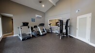 Located at 700 Martin Creel Blvd in Summerville, South Carolina, this fitness center is a well-equipped, single-floor facility designed to support a well-rounded exercise routine. The space features soaring vaulted ceilings that lend an open, airy feel, while neutral gray walls and durable rubber flooring create a clean, functional environment suited for active use.

The cardio section is outfitted with multiple treadmills — including Matrix-branded units — along with a recumbent bike and an elliptical trainer, providing a variety of options for cardiovascular workouts. A multi-function cable resistance machine rounds out the strength training offerings, accommodating a range of exercises for users of all fitness levels. A wall-mounted split-system air conditioning unit ensures a comfortable climate year-round.

Natural light fills the space through multiple windows along the walls, and a large mirror panel enhances the sense of openness. A standout architectural feature is the expansive glass wall and door system on one side of the fitness center, offering direct views of the outdoor swimming pool and surrounding grounds — creating a bright, inviting atmosphere that connects the interior with the outdoor amenity area. A clearly posted Fitness Center rules sign ensures proper use of the facility. The space is accessible via a dedicated entry door, making it a convenient and well-appointed amenity.