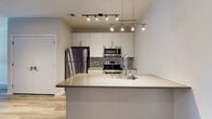 Located at The Hub in Philadelphia's vibrant Strawberry Mansion neighborhood, this single-floor unit showcases a clean, modern design with thoughtful finishes throughout. The open-concept layout flows seamlessly from the living area to the kitchen, anchored by warm hardwood-style flooring and a striking deep-purple accent wall that adds a bold visual element to the main living space.

The kitchen is a standout feature, equipped with a full suite of stainless steel appliances including a refrigerator, electric range, and over-the-range microwave. Crisp white cabinetry extends to the ceiling, maximizing storage, while a mosaic tile backsplash adds texture and depth. A large center island with a smooth quartz-style countertop and undermount sink provides additional prep space and serves as a natural gathering point. Overhead, dual track and pendant lighting systems illuminate the kitchen with both functionality and style.

The bedroom offers a comfortable, carpeted retreat with neutral tones, and a window with access to a sliding glass door allows for natural light and outdoor connectivity. The bathroom is outfitted with a full tub and shower combo enclosed by sliding frameless glass doors, set above classic tile flooring. The unit's layout, contemporary palette, and quality finishes make it a well-appointed urban residence.