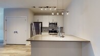 Located at The Hub in Philadelphia's vibrant Strawberry Mansion neighborhood, this single-floor unit showcases a clean, modern design with thoughtful finishes throughout. The open-concept layout flows seamlessly from the living area to the kitchen, anchored by warm hardwood-style flooring and a striking deep-purple accent wall that adds a bold visual element to the main living space.

The kitchen is a standout feature, equipped with a full suite of stainless steel appliances including a refrigerator, electric range, and over-the-range microwave. Crisp white cabinetry extends to the ceiling, maximizing storage, while a mosaic tile backsplash adds texture and depth. A large center island with a smooth quartz-style countertop and undermount sink provides additional prep space and serves as a natural gathering point. Overhead, dual track and pendant lighting systems illuminate the kitchen with both functionality and style.

The bedroom offers a comfortable, carpeted retreat with neutral tones, and a window with access to a sliding glass door allows for natural light and outdoor connectivity. The bathroom is outfitted with a full tub and shower combo enclosed by sliding frameless glass doors, set above classic tile flooring. The unit's layout, contemporary palette, and quality finishes make it a well-appointed urban residence.