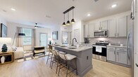 This 2-bedroom, 3-bathroom residence offers a smartly designed single-floor layout that maximizes both functionality and style. The open-concept kitchen and living area serves as the heart of the home, anchored by a large center island with granite countertops, a built-in sink, and seating for multiple guests. Pendant lighting with matte black fixtures hangs above the island, complementing the gray shaker-style cabinetry and stainless steel appliances, including a refrigerator, range, and microwave. Light wood-look flooring flows throughout the main living areas, enhancing the bright, airy atmosphere created by white walls and abundant natural light. The living room features a ceiling fan, large windows, and a glass door that opens to a private outdoor area. Each bedroom is carpeted and comfortably scaled, with the primary bedroom offering direct access to an en suite bathroom featuring a double vanity with granite countertops, gray cabinetry, and wood-look tile flooring. A spacious walk-in closet with wire shelving provides generous storage. The secondary bedroom is served by its own well-appointed bathroom. A third bathroom adds additional convenience. Two closets across the unit ensure ample storage throughout this polished and cohesive living space.