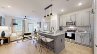 This 2-bedroom, 3-bathroom residence offers a smartly designed single-floor layout that maximizes both functionality and style. The open-concept kitchen and living area serves as the heart of the home, anchored by a large center island with granite countertops, a built-in sink, and seating for multiple guests. Pendant lighting with matte black fixtures hangs above the island, complementing the gray shaker-style cabinetry and stainless steel appliances, including a refrigerator, range, and microwave. Light wood-look flooring flows throughout the main living areas, enhancing the bright, airy atmosphere created by white walls and abundant natural light. The living room features a ceiling fan, large windows, and a glass door that opens to a private outdoor area. Each bedroom is carpeted and comfortably scaled, with the primary bedroom offering direct access to an en suite bathroom featuring a double vanity with granite countertops, gray cabinetry, and wood-look tile flooring. A spacious walk-in closet with wire shelving provides generous storage. The secondary bedroom is served by its own well-appointed bathroom. A third bathroom adds additional convenience. Two closets across the unit ensure ample storage throughout this polished and cohesive living space.