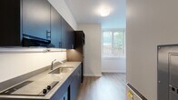 Located in Seattle's vibrant Phinney Ridge neighborhood, Unit 17 at 3635 Phinney Ave N is a thoughtfully designed single-floor unit offering a clean, modern aesthetic throughout. The space features durable wood-look flooring that runs continuously, tying each area together with a cohesive, contemporary feel.

The kitchenette is a standout feature, outfitted with bold navy cabinetry extending from floor to ceiling, providing ample storage. A light-toned countertop with an undermount sink, a built-in cooktop, microwave, and a full-size refrigerator make this kitchen both functional and stylish. Under-cabinet lighting adds a warm, practical glow to the workspace. Wall-mounted shelving near the entry offers additional storage options.

The main living area is bright and open, benefiting from a large window that frames views of surrounding greenery and a wooden fence, inviting natural light deep into the space. The neutral white walls and clean lines create a calm, airy ambiance.

The bathroom is well-appointed with an open walk-in shower featuring a minimalist surround, a grab bar for accessibility, and a modern toilet — all finished in a clean, light palette that complements the rest of the unit. The consistent wood-look flooring extends into this space as well.

Overall, Unit 17 presents a compact yet efficiently utilized layout with modern finishes, making it a functional and stylish option in the heart of Seattle.
