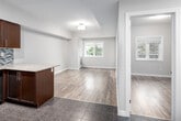 This well-appointed 2-bedroom, 2-bathroom unit at 5 Rittenhouse Road in Kitchener, Ontario offers a thoughtfully designed single-floor layout. The open-concept kitchen and living area serves as the heart of the home, featuring rich dark wood cabinetry, granite countertops, a mosaic tile backsplash, stainless steel appliances including a dishwasher, and a peninsula that provides additional counter space and separates the kitchen from the living area. Track lighting above the kitchen adds a modern touch, while a flush ceiling fixture illuminates the adjacent living space. Durable wood-look laminate flooring flows throughout the main living areas, complemented by tile flooring in the kitchen and bathrooms. The spacious primary bedroom benefits from a natural light through a window and includes a private ensuite bathroom equipped with a sliding glass shower and a granite-topped vanity with dark wood cabinetry. The second bathroom features a soaker tub with shower combo and a matching granite vanity. The second bedroom is generously sized with hardwood-look flooring and a bright window. A hallway reveals a practical in-unit stacked washer and dryer. Neutral tones throughout create a clean, modern ambiance ideal for comfortable living.