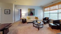 Located at 410 Blake St in New Haven, CT, this single-floor residence offers a well-planned layout with a variety of comfortable living spaces. The open living room features plush carpeting, neutral tones, and large windows that invite generous natural light, creating a bright and welcoming atmosphere. A second seating area provides additional flexibility and flows seamlessly toward the kitchen and dining spaces.

The kitchen is equipped with warm wood cabinetry, dark granite-style countertops, wood-look flooring, and a full suite of black appliances, including a range, microwave, and refrigerator — offering ample storage and counter space for everyday use.

The residence includes multiple bedrooms, each distinctly styled. One bedroom features bold crimson walls and a dramatic four-poster bed frame with large windows on two sides. Another offers a serene, earthy palette with a dark wood headboard and soft aqua accents, complemented by natural light from a wide window framing outdoor greenery.

The bathrooms are finished with wood-look flooring and clean tile work. The primary bathroom includes a walk-in tiled shower and direct access to a spacious walk-in closet, while a secondary bathroom features a full tub-shower combination. Together, these spaces present a cohesive, comfortable home with thoughtful finishes throughout.