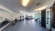 This single-level fitness center is designed to support a comprehensive workout experience, offering a thoughtfully organized layout with a wide variety of equipment. The space is finished with durable, dark rubber flooring throughout, providing both safety and functionality for high-intensity use.

The cardio zone is prominently featured along one wall, housing multiple treadmills and an elliptical trainer, each equipped with individual screens for entertainment during workouts. Stationary cycling bikes and a rowing machine round out the cardio offerings, providing options for varied aerobic training.

On the strength side, the space includes a Matrix functional trainer and cable system, a adjustable weight bench, a full rack of dumbbells, and a hanging punching bag, accommodating a broad range of strength and conditioning exercises.

A large wall mirror visually expands the space and aids in form monitoring during workouts. Natural light filters in through multiple windows, creating a bright and energizing atmosphere. Overhead, recessed flush-mount lighting ensures consistent illumination throughout.

A bold, horizontally striped accent wall in tones of teal, green, and white adds a vibrant, modern visual element, distinguishing this fitness center with a lively, welcoming aesthetic.
