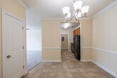 This single-floor residence offers a thoughtfully designed layout with a warm, neutral color palette throughout. The entryway welcomes visitors with elegant crown molding and light tile flooring, illuminated by a decorative chandelier that also graces the adjacent dining area. The dining space flows seamlessly into the kitchen, which is outfitted with warm-toned wood cabinetry, granite countertops, tile flooring, and black appliances including a full-size refrigerator and dishwasher. A utility panel is conveniently located within the kitchen corridor. The generously proportioned living room features plush carpeting, crown molding, a ceiling fan with light fixture, and a wide window that invites natural light and outdoor views. Multiple bedrooms continue the carpet-and-crown-molding theme, each offering windows with blinds for natural light and privacy. The two bathrooms are finished with granite-topped vanities and tile flooring. One bathroom includes a walk-in shower equipped with accessibility grab bars, while the other features a full soaking tub and shower combination. Throughout the residence, clean white baseboards and soft cream walls create a bright, cohesive, and move-in-ready atmosphere.