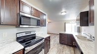 This two-story residence offers a thoughtfully designed layout that balances functionality and style across both levels. The kitchen serves as a central highlight, featuring rich dark-stained cabinetry with sleek hardware, light stone-finish countertops, and a full suite of stainless steel appliances, including an electric range and an over-the-range microwave. The cabinetry extends to a kitchen island or peninsula with additional drawer storage, providing ample workspace and organization. The kitchen flows seamlessly into an adjacent living area, creating an open, connected atmosphere ideal for everyday living and entertaining. Durable wood-look flooring runs throughout the main level, adding warmth and continuity to the space. Natural light filters in through a sliding glass door or large window in the living area, brightening the interior and offering a view to the outdoors. A chandelier-style light fixture adds a touch of elegance to the dining or living zone. The textured ceilings and neutral wall tones throughout provide a clean, move-in-ready backdrop. With its open-concept design and modern finishes, this two-story home delivers a comfortable and practical living environment.