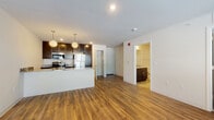 This single-floor unit at 417 Church Ave in Verona, Wisconsin offers a well-designed, modern living space with a cohesive open-concept layout. The main living and kitchen area is unified by warm hardwood-style flooring that extends throughout, creating a seamless and visually spacious environment. Large windows and a glass-paneled exterior door flood the living area with natural light while providing access to a private outdoor space with railing detail.

The kitchen is a standout feature, anchored by a peninsula with granite countertops that serves as both a functional workspace and a casual dining or gathering spot. Globe pendant lights hang above the peninsula, complementing the rich dark cabinetry that extends to the ceiling. Stainless steel appliances — including a refrigerator, range, and microwave — complete the kitchen's modern, polished aesthetic.

Adjacent to the main living space, a bedroom features plush carpet flooring and a sliding-door closet with built-in wire shelving for organized storage. The bathroom is finished with neutral tile flooring, a granite-topped dark vanity, and a full tub-shower combination. A dedicated in-unit laundry area with a stacked washer and dryer adds everyday convenience. The space maintains a clean, contemporary feel throughout.