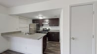 This single-floor, 2-bedroom, 2-bathroom residence is thoughtfully laid out to maximize comfort and functionality. Dark espresso-toned cabinetry anchors the kitchen, which is equipped with stainless steel appliances including a refrigerator and electric range. A peninsula counter with a built-in sink provides additional prep space and creates a natural divide between the kitchen and the adjacent living area. Wood-look flooring runs consistently throughout the main living spaces, offering a cohesive and durable aesthetic. A sliding glass door in the living area allows natural light to filter in and provides access to an outdoor space. Both bedrooms are generously proportioned, each featuring large windows with blinds that bring in natural light, ceiling fans with integrated lighting, and the same rich wood-look flooring. The clean, neutral wall tones in each bedroom create a calm, versatile backdrop. The bathrooms include a full tub-shower combination with white tile surround and chrome fixtures, maintaining a clean and practical finish. Textured ceilings are present throughout the unit. The overall design is straightforward and functional, offering a well-balanced living environment suitable for a variety of lifestyles.