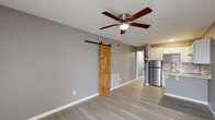 Located at 101 S Genoa St in South Houston, TX, this efficiently designed unit offers a thoughtful layout across a single floor. The open living area greets you upon entry with neutral gray walls, light wood-style vinyl flooring, and a ceiling fan that enhances comfort year-round. A window near the front door allows natural light to brighten the space, creating an airy feel despite the compact footprint.

The kitchen is a standout feature, showcasing white shaker-style cabinetry, a gray subway tile backsplash, and light stone-finish countertops. A stainless steel refrigerator, built-in cooktop, and under-cabinet range hood provide full cooking functionality. A peninsula counter with a drop-leaf extension adds casual dining or workspace versatility, seamlessly connecting the kitchen to the living area.

The bathroom is clean and contemporary, finished with large-format gray tile in a walk-in shower stall with a built-in niche and a frameless glass enclosure. Mosaic tile flooring and recessed lighting complete the polished look.

A barn-style interior door adds a rustic design accent, while a dedicated thermostat and multiple HVAC vents ensure climate control throughout. This unit delivers a well-appointed, move-in ready space with modern finishes in a practical, efficient layout.