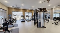 Located at 1000 Vintage Brunswick Cir in Brunswick, Georgia, this fitness center offers a comprehensive and thoughtfully designed exercise space across a single expansive floor. The interior design blends modern aesthetics with functional practicality, highlighted by warm wood-paneled accent walls, neutral-toned painted walls, and durable speckled flooring suited for high-traffic athletic use. Multiple ceiling fans are distributed throughout, promoting airflow and comfort during workouts, while recessed lighting ensures the space is well-lit at all times.

Large floor-to-ceiling windows line the perimeter, inviting abundant natural light and providing views of the surrounding outdoor amenities, including what appears to be a pool area and landscaped grounds. The cardio zone is generously appointed with multiple treadmills, elliptical trainers, stationary bikes — including Peloton-style cycles — and a rowing machine, many equipped with interactive display screens. The strength training area features a TAG cable machine, a full power rack, a comprehensive dumbbell rack, medicine ball storage, and multiple adjustable benches. Full-length mirrors in the strength zone enhance spatial awareness during training. The space also includes a dedicated area for cycling and stair-climbing equipment, rounding out a truly versatile fitness facility.