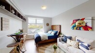 Located at 1231 NW 19th Ave in Portland's Northwest District, this single-level studio offers a well-designed open layout that efficiently combines living and sleeping areas. Light wood-tone flooring runs throughout, creating a warm, cohesive aesthetic.

The main living area is bright and airy, anchored by a large window that frames views of the surrounding Portland rooftops and greenery, allowing abundant natural light to fill the space. The open floor plan comfortably accommodates both a sleeping area and a dedicated living zone, with a built-in closet providing organized storage.

The kitchen is compact yet fully functional, equipped with stainless steel appliances including a refrigerator, electric range, built-in microwave, and dishwasher. Warm wood cabinetry pairs with light countertops and a white subway tile backsplash, lending a modern, clean look.

The full bathroom features wood-toned cabinetry with a single vanity, a large wall mirror with overhead lighting, and a shower/tub combination. Wood-look flooring continues here, complementing the neutral gray walls.

An entry corridor connects all areas smoothly, contributing to the unit's efficient and functional flow. The overall ambiance is contemporary and understated, well-suited to urban living in Portland.