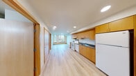 Unit 413 at 1801 E Yesler Way in Seattle's Central District offers a well-organized one-bedroom, one-bathroom layout across a single floor. Light wood-style flooring runs throughout the entire unit, providing a clean, cohesive aesthetic. The open living area is bright and functional, benefiting from recessed lighting and a neutral color palette. The kitchen is positioned along one wall and features warm wood cabinetry with ample upper and lower storage, dark countertops, a white electric range, dishwasher, refrigerator, and a single-basin sink — all well-appointed for everyday use. The bedroom is a comfortable, enclosed space with corner windows that invite natural light and offer views of the surrounding Seattle neighborhood. A closet with a hanging rod provides built-in storage. The bathroom includes a wood-toned vanity with under-sink storage, a full bathtub, and a toilet, finished with the same light flooring found throughout the unit. A dedicated closet area adjacent to the bathroom offers additional storage. The unit's layout is efficient and straightforward, with interior doors featuring contemporary wood finishes that complement the overall design. Recessed lighting throughout ensures consistent illumination in every room.