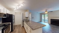 Located at 100 Eclipse Dr in Cary, NC, this single-floor residence offers a well-designed open-concept layout that seamlessly connects the kitchen, dining, and living areas. The kitchen is outfitted with white cabinetry, granite countertops, a peninsula with an undermount sink, stainless steel appliances including a refrigerator, range, and microwave, and track lighting overhead. Wood-look flooring runs throughout the main living areas, lending warmth and continuity to the space.

The living room is a standout feature, centered around a tile-surround fireplace with a classic white mantel. A ceiling fan adds comfort, and a sliding glass door opens to a private balcony with outdoor views, allowing natural light to pour in. An additional window further brightens the room.

The bedrooms are carpeted for comfort, each offering generous proportions and natural light from windows. One bedroom includes a walk-in closet with built-in shelving. The bathroom echoes the kitchen's design language with granite countertops, an undermount sink, white cabinetry, and wood-look flooring. A large mirror above the vanity enhances the sense of space. The textured ceilings are consistent throughout, and the neutral color palette creates a clean, cohesive aesthetic across the entire residence.