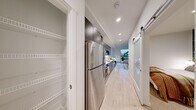 Located in Seattle's historic Pioneer Square neighborhood, this thoughtfully designed one-bedroom, one-bathroom residence offers a clean, modern aesthetic with warm, inviting touches throughout. Light wood-tone flooring runs continuously through the space, complementing the crisp white walls and recessed lighting that keep each room bright and airy.

The living room serves as the heart of the home, anchored by oversized windows that frame treetop and city views, flooding the space with natural light. The galley-style kitchen is efficiently appointed with gray shaker cabinetry extending to the ceiling, stainless steel appliances including a full-size refrigerator, gas range, dishwasher, and microwave, all set against a classic white subway tile backsplash with quartz countertops.

A long hallway connects the living areas to the private bedroom, which features a striking botanical-print accent wall that adds depth and character to the cozy retreat. A dedicated closet with built-in shelving provides organized storage. The bathroom is finished with a sleek floating vanity in gray, a white quartz countertop, large mirror, and in-unit laundry. A sliding barn door and clean architectural lines complete this well-planned, contemporary Seattle residence.