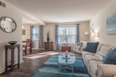 Located at 12487 Warwick Blvd in Newport News, Virginia, this single-floor residence offers a thoughtfully laid-out floor plan with comfortable living spaces throughout. The living room features warm hardwood-style flooring, neutral walls, and natural light streaming through large windows dressed with elegant drapes and blinds, creating an inviting, relaxed atmosphere. A pendant-lit dining area flows seamlessly from the living space, with hardwood-style flooring continuing throughout for a cohesive look. The kitchen is well-equipped with abundant oak cabinetry, ample counter space, a double-basin sink, an electric range, a dishwasher, and tile flooring — with convenient in-unit laundry hookups visible nearby. The primary bedroom is generously sized with plush carpeting, a wide closet, and windows allowing ample natural light. A second bedroom also features carpet flooring and a spacious closet, offering versatile use. Two bathrooms serve the unit: one with tile flooring, a vanity with wood cabinetry, and a shower/tub combination, and a second with tile flooring and a clean, functional layout. Throughout the space, neutral tones, tile, and wood-style flooring unify the design, offering a practical and comfortable living environment.