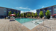 Located at 1311 Holling Pl in Frederick, Maryland, this outdoor amenity space serves as a central gathering area within a multi-building residential community. The centerpiece is a generously sized, crystal-clear swimming pool with a shallow entry point and built-in in-water lounge chairs, ideal for relaxing on warm days. The pool area is finished with attractive paver-style decking that surrounds the water on multiple sides, providing ample space for sunbathing and socializing.

Surrounding the pool, a well-appointed sundeck is furnished with numerous lounge chairs and shaded seating areas accented by red umbrellas and potted greenery, creating a vibrant and welcoming atmosphere. The pool is enclosed by a black wrought-iron fence, ensuring safety and defined boundaries within the outdoor space.

Anchoring one side of the pool area is a two-story clubhouse structure with a pitched roof, stone chimney, and large windows that look out onto the deck. The building appears to offer additional indoor amenities and direct access to the pool area through glass doors. Mature trees are interspersed throughout the courtyard, providing natural shade and privacy. The surrounding multi-story residential buildings frame the space, creating an enclosed, resort-like environment perfect for outdoor recreation and relaxation.
