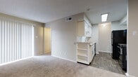 This single-floor residence is designed with a clean, neutral aesthetic that creates a bright and cohesive atmosphere throughout. The open-concept living area is finished with plush wall-to-wall carpeting and features a sliding glass door dressed with vertical blinds, allowing ample natural light to fill the space. A textured ceiling and central HVAC venting contribute to a comfortable, well-ventilated environment.

The kitchen is efficiently arranged and connects seamlessly to the living area via a peninsula with open shelving below. White cabinetry with brushed nickel hardware pairs with light granite-style countertops and a classic white subway tile backsplash. A stainless steel sink with a modern pull-down faucet, a black dishwasher, and a stainless steel refrigerator complete the kitchen's functional layout. Wood-look flooring extends through the kitchen and into adjacent areas, providing a durable contrast to the carpeted living spaces.

The bedroom is generously proportioned, featuring soft carpeting, a ceiling fan, and a window with blinds for natural light and privacy. The entry area transitions smoothly from wood-look flooring to carpet, with a closet conveniently located near the front door. The bathroom includes a tiled shower-tub combination, wood-look flooring, and a vanity with matching granite-style countertops, maintaining design consistency throughout the home. An in-unit laundry area adds everyday convenience.