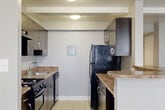 Located at 1002 Kennebec St in Oxon Hill, MD, this single-floor residence offers two bedrooms, two bathrooms, and a thoughtfully arranged layout designed for comfortable everyday living. The entrance leads into a combined living and dining area featuring plush carpeting, neutral gray walls, and multiple windows fitted with blinds that allow for ample natural light. A ceiling fan adds both style and functionality to the living space, which also includes a wall-mounted HVAC unit for year-round climate control. The kitchen is efficiently designed with a galley-style configuration, featuring dark espresso cabinetry, granite-look countertops, tile flooring, and a full suite of black appliances including a gas range, dishwasher, and refrigerator. The primary bedroom is generously proportioned, carpeted, and includes two side-by-side closets offering abundant storage. The second bedroom is similarly finished with carpet flooring, a large window, and its own wall HVAC unit. Four closets are distributed throughout the unit, providing excellent storage capacity. Both bathrooms are clean and functional, with one featuring a full tub-shower combination with white tile surround. The overall aesthetic is understated and neutral, offering a move-in ready canvas throughout.