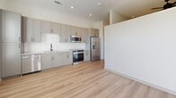 Located in Suwanee, GA, this thoughtfully designed 2-bedroom, 1-bathroom unit on McGinnis Ferry Road offers a clean, modern aesthetic throughout its single-floor layout. The entrance opens into a bright hallway with light wood-look flooring that carries through the main living areas, creating a cohesive and airy feel. The kitchen is a standout feature, outfitted with gray shaker-style cabinetry, a white subway tile backsplash, granite-look countertops, stainless steel appliances including a refrigerator with ice maker, range, microwave, and dishwasher. Recessed lighting enhances the crisp, contemporary atmosphere. Both bedrooms are carpeted for comfort and feature ceiling fans. The primary bedroom includes a built-in closet with modern gray cabinetry and an additional double-door closet, providing ample storage. The full bathroom is finished with large-format tile in the tub/shower surround, matte black hardware accents, a vanity with stone-look countertop, and wood-look tile flooring. A dedicated laundry area adds everyday convenience. The overall design is clean and neutral, with white walls and modern hardware finishes tying the space together seamlessly.