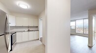 Located at 1140-1150 Fisher Ave in Ottawa, Ontario, this thoughtfully laid-out unit offers a comfortable and functional single-floor living space. The open-concept design integrates the kitchen and living room seamlessly, making efficient use of every square foot.

The kitchen is a standout feature, finished with crisp white shaker-style cabinetry extending to the upper walls for generous storage. A classic white subway tile backsplash complements the dark countertops, while a stainless steel electric range and double sink add practical utility. Light-toned tile flooring grounds the kitchen area with a clean, modern aesthetic.

The living area transitions smoothly from the kitchen, showcasing warm natural wood-tone laminate flooring that adds a welcoming character to the space. Neutral, off-white walls keep the interior bright and versatile. A large floor-to-ceiling window wall is the defining architectural feature of the living room, flooding the space with natural light and offering expansive elevated views of the Ottawa cityscape and surrounding neighbourhood — a truly notable highlight of this unit.

A hallway connects the main living areas to additional spaces, including closet storage. The overall palette throughout is clean and contemporary, with warm neutrals creating a calm, move-in-ready ambiance suited to a variety of lifestyles.