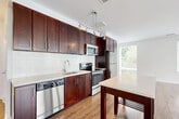 Located at 3445 Berkeley St, Unit 445 in Alexandria, VA, this well-appointed 2-bedroom, 2-bathroom residence offers a thoughtfully designed single-floor layout. A clean, well-lit hallway with light wood flooring provides a welcoming entry, leading into the open-plan combined living and dining area. The living room is expansive and bright, featuring wide hardwood-style flooring and large windows with views of the surrounding greenery, flooding the space with natural light.

The kitchen is a standout feature, showcasing rich dark wood cabinetry that extends to the ceiling, a classic white subway tile backsplash, light stone countertops, and a full suite of stainless steel appliances including a dishwasher, range, microwave, and refrigerator. A pendant track light fixture adds a contemporary touch, and the adjacent dining area provides convenient, open access.

Both bedrooms are comfortably sized, finished with plush carpeting and crisp white walls. The primary bedroom offers generous proportions. Two full bathrooms feature light tile flooring, dark wood vanities with white countertops, large mirrors, and clean, modern fixtures — one with a tiled walk-in shower. Additional conveniences include four closets and a dedicated laundry area, completing this functional and modern Alexandria residence.