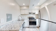 This single-floor residence offers a well-organized layout with a clean, neutral aesthetic throughout. The kitchen is a standout feature, showcasing white shaker cabinetry, granite countertops with subtle grey and white veining, light hardwood-style flooring, and a full suite of stainless steel appliances including a gas range, refrigerator, and dishwasher. A recessed lighting system and under-cabinet range hood add both functionality and a modern finish to the space.

The living area is generously proportioned, finished with plush wall-to-wall carpeting and neutral grey-toned walls. A ceiling fan with integrated lighting provides comfort and airflow. A large window with vertical blinds allows natural light to fill the room, while a front entry door opens directly into this open space.

The bedroom is comfortably sized with carpeted flooring, a window with an outdoor view, and access to a walk-in closet featuring a full-width shelving rod for organized storage.

The bathroom is finished with white marble-style tile extending across the floor and tub surround, complemented by a white vanity with a mirrored medicine cabinet and a multi-bulb vanity light fixture, creating a bright, clean environment.