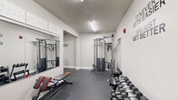 Located at 200 East 5th Avenue in York, Pennsylvania, this fitness center is a thoughtfully designed facility spread across a single floor. The space is divided into two dedicated exercise rooms connected by a hallway, offering a focused and functional workout environment.

The main exercise room features durable rubber-speckled flooring and is outfitted with a multi-function cable machine, a full dumbbell rack with a wide range of weights, and an adjustable workout bench. Large wall mirrors visually expand the space, while motivational wall decals energize the atmosphere. Overhead fluorescent lighting ensures the area is well-lit throughout. A wall-mounted split air conditioning unit provides climate control for user comfort.

The secondary exercise room includes a spin bike with a wall-mounted flat-screen TV, treadmills, a stair climber, and additional accessories stored on a rolling utility rack. Motivational phrases such as "Stay Positive, Work Hard, Make It Happen" and "Stronger Than Yesterday" are prominently displayed across the neutral-toned walls, reinforcing an encouraging training environment.

Both rooms share a cohesive aesthetic of clean white walls and grey rubber flooring, creating a modern, no-frills atmosphere built for performance. A hallway connects the two rooms and provides access to the facility entrance, contributing to a smooth and efficient layout throughout the space.