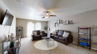 This single-floor residence is thoughtfully designed for comfortable, everyday living, featuring an open-concept layout that connects the kitchen, dining, and living areas into one cohesive space. The kitchen is equipped with warm wood cabinetry, dark countertops, black appliances including a full-size refrigerator, electric range, and over-the-range microwave, all set atop durable tile flooring. A peninsula with an overhang provides casual bar seating with pendant lighting above, making it ideal for quick meals or entertaining. The open layout flows seamlessly into a dedicated dining nook and a spacious living room, where plush carpeting, a ceiling fan with light fixture, and sliding door access to natural light create a warm, inviting atmosphere. Two bedrooms offer carpeted floors and ample closet storage, with ceiling fans providing added comfort. One bedroom features a sliding closet and a window with sheer curtains, while the other includes generous floor space. The full bathroom includes a tub-shower combination with chrome fixtures and wood-toned cabinetry. A dedicated laundry area with a full-size washer and dryer and built-in shelving adds everyday convenience. Throughout, the neutral color palette and textured ceilings lend a clean, cohesive aesthetic.