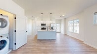 Located at 400 East Genesee Pointe Drive in Henrietta, NY, this single-floor home offers a thoughtfully designed layout with one bedroom, one kitchen, and a living room. The open-concept kitchen is a standout feature, boasting crisp white shaker cabinetry extending to the ceiling, stainless steel appliances including a side-by-side refrigerator, a built-in microwave, and a range. A central island with a light countertop and pendant lighting serves as both a functional workspace and a focal point of the space. Light hardwood-style flooring flows throughout the main living areas, lending warmth and continuity. The living area is bright and airy, benefiting from natural light streaming through multiple windows with views of the surrounding neighborhood. A conveniently positioned stacked washer and dryer unit adds practical in-unit laundry. The generously sized primary bedroom features plush carpeting, dual windows that invite abundant natural light, and a closet with built-in shelving and rod storage. The overall aesthetic is clean and contemporary, with white walls, modern black hardware accents, and recessed lighting creating a bright, welcoming atmosphere throughout.