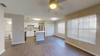This well-appointed single-floor residence offers a thoughtfully designed open-concept layout that seamlessly connects the kitchen, dining, and living areas. The kitchen is a standout feature, outfitted with crisp white cabinetry, a subway tile backsplash, stainless steel appliances including a refrigerator, range, microwave, and dishwasher, and a central island that provides additional prep space and casual seating. Wood-look flooring flows throughout the main living areas, adding warmth and visual continuity.

The living area is generously proportioned and bathed in natural light, courtesy of large windows dressed with white blinds. A ceiling fan overhead enhances comfort and airflow. A closet with louvered doors provides convenient built-in storage near the main living space.

A secondary room features soaring vaulted ceilings and an arched transom window above standard windows, creating an airy and dramatic atmosphere filled with natural light. Additional bedrooms offer wood-look flooring and natural light through side windows. The bathroom is clean and functional, featuring white shaker-style cabinetry, a white countertop vanity, a large mirror, and a shower-tub combination. The textured ceilings and neutral warm-toned walls tie the space together with a cohesive, move-in-ready aesthetic.