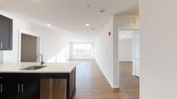 Located at 100 Town Center Blvd in Sewell, NJ, this single-floor unit offers a clean, modern aesthetic throughout. The open-concept living area features warm hardwood-style flooring and crisp white walls that maximize the sense of space and light, with a large window at the far end of the main living area drawing in generous natural light.

The kitchen is a standout feature, showcasing dark espresso cabinetry contrasted by white quartz countertops and a classic subway tile backsplash. A full suite of stainless steel appliances — including a refrigerator, electric range, microwave, and dishwasher — is complemented by a kitchen island with sink, providing ample prep and storage space.

The bedroom is well-proportioned, offering hardwood-style flooring and access to a spacious walk-in closet with built-in shelving and hanging rods. The bathroom is elegantly finished with a dual-sink vanity featuring dark cabinetry, a wide framed mirror, white tile surround, and a full tub-shower combination with mosaic accent tile detailing.

Throughout the unit, recessed lighting, white panel doors, and neutral tones create a cohesive, contemporary feel. The thoughtful layout connects living, dining, and kitchen spaces seamlessly, making this a highly functional and inviting residence.