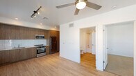 This thoughtfully designed single-floor unit offers a clean, contemporary aesthetic throughout. The open-concept living and kitchen area is anchored by light hardwood-style flooring and a ceiling fan, creating an airy, comfortable atmosphere. Large windows flood the living space with natural light and provide views of the surrounding neighborhood, while a glass door opens to a private balcony, extending the living area outdoors.

The kitchen is well-appointed with warm wood-grain cabinetry, white quartz countertops, and a glossy white subway tile backsplash. Stainless steel appliances — including a refrigerator, electric range with oven, and an over-the-range microwave — provide a full suite of modern conveniences. Track lighting above the kitchen adds focused illumination to the workspace.

The bedroom is a quiet retreat, finished with plush carpeting, a ceiling fan, and a window with blinds that overlooks the exterior. A closet provides practical storage directly off the room.

The full bathroom is finished with wood-grain cabinetry, a white undermount sink with quartz countertop, a large mirror with modern vanity lighting, and a combination tub and shower. Light hardwood-style flooring carries through the bathroom, maintaining a cohesive look across the unit. Clean white walls throughout contribute to the bright, modern feel of the space.