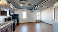Located at 1625 Perry St in Denver's vibrant West Colfax neighborhood, this studio unit delivers an urban industrial aesthetic within a thoughtfully efficient single-floor layout. The open living area features warm wood-style flooring throughout and crisp white walls that contrast with the dramatic dark-painted ceiling showcasing exposed metal ductwork and track lighting — a defining architectural detail that adds character and visual height to the space. Multiple windows along the main living area flood the unit with natural light while offering views of the surrounding neighborhood. A wall-mounted HVAC unit provides climate control. The kitchen is well-appointed with dark espresso cabinetry extending floor to ceiling, light countertops, a stainless steel sink, and a full suite of black appliances including a refrigerator, electric range, built-in microwave, and dishwasher. The entryway features a solid gray steel door with a secure lever-handle lock, offering a clean and modern first impression. The full bathroom includes a tub/shower combination with white tile surround, a dark vanity with undermount sink, open shelving for storage, and the same wood-style flooring found throughout the unit. This space combines functional design with distinctive industrial styling in a prime Denver location.