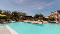 The pool area is a well-appointed outdoor amenity space designed for relaxation and recreation. The centerpiece is a large, rectangular swimming pool with clear turquoise water, accessible via stainless steel handrails and steps. Adjacent to the main pool is a spa, providing an additional leisure option for residents.

The surrounding deck is finished in a smooth concrete surface, offering ample space for lounge chairs and seating arrangements positioned to take advantage of open sky views. A wooden pergola provides a shaded gathering spot, complementing the yellow market umbrellas stationed throughout the deck for additional sun coverage. Decorative planters and mature trees border the area, adding greenery and a sense of privacy to the space.

The pool area is enclosed by a wrought iron fence and accessed through a dedicated entrance with dark-framed glass doors and a wall-mounted exterior light fixture. Posted pool rules are visible near the entry point. The facility is framed by a multi-story residential building, offering direct pool views from adjacent patios and balconies. The overall ambiance is open, bright, and inviting, suitable for warm-weather outdoor enjoyment.