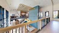 This expansive 3,340 square foot commercial space in Suwanee, GA, showcases a striking blend of modern architecture and artistic flair. The interior is characterized by an open, multi-level design with high ceilings and ample natural light from large windows. A standout feature is the dramatic blue abstract mural that spans an entire wall, adding a bold splash of color to the crisp white interiors.

The space incorporates a mezzanine level with sleek wood and metal railings, offering additional functional areas and visual interest. Wooden lattice ceiling features and curved LED light fixtures add warmth and sophistication to the overall design. The color scheme primarily consists of white, natural wood tones, and strategic pops of blue and yellow.

A spacious kitchen area features blue cabinetry, a large concrete-topped island, and modern pendant lighting. Comfortable seating areas are scattered throughout, with plush leather sofas and stylish chairs. The overall ambiance is one of contemporary elegance, perfect for a modern office, creative studio, or upscale retail environment. The thoughtful design seamlessly blends functionality with aesthetic appeal, creating an inviting and inspirational atmosphere for work or leisure.