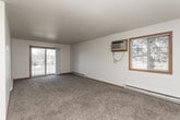 This single-floor unit offers a practical and well-organized layout across several distinct living spaces. The open-concept main area seamlessly connects the living room and kitchen, with a transition from durable tile flooring in the kitchen to plush carpeting in the living space. The living room is generously sized, featuring a textured ceiling, a baseboard heating unit, and a sliding glass door that opens to a private balcony, offering views of the surrounding neighborhood. Natural light filters in comfortably through this access point.

The kitchen is arranged in a galley-style configuration, equipped with warm honey-toned wood cabinetry, dark granite-style countertops, a double stainless steel sink, a black dishwasher, a black refrigerator, and matching appliances. Tile flooring completes the functional workspace.

The bedrooms are carpeted and feature ceiling fans and sliding wood-panel closet doors providing ample storage. A window unit air conditioner and baseboard heater are present in the primary bedroom, which also receives natural light from a wood-framed window.

The bathroom includes tile flooring, a wood vanity with dark countertop, a full tub and shower surround, and grab bars for accessibility. Throughout the unit, warm wood trim and neutral walls contribute to a cohesive, understated aesthetic.